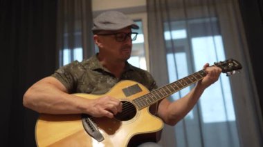 Orta yaşlı bir adam akustik gitar çalıyor, yeni bir hobi için pratik yapıyor.