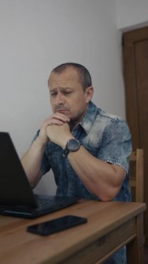 Evdeki masasında dizüstü bilgisayarını kullanan bir adam.