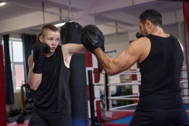 Güçlü genç kickboksör kickboks salonunda koçla pedlere vuruyor.