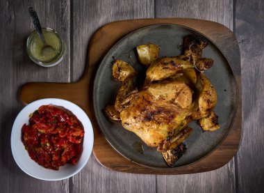 Tavuğun tamamı ahşap bir tabakta ızgara ve biber turşusu ve sarımsak sosuyla.