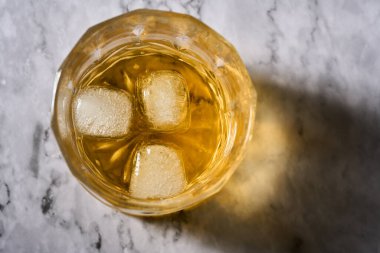 Mermer zemin üzerinde buz olan bir bardak viskinin yakın çekimi.