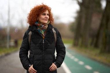 Kıvırcık saçlı kadın soğuk bir kış gününde parkta yürüyor.