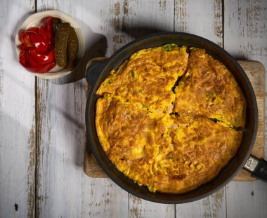 Tahta bir masada kırmızı biber ve salatalıkla servis edilen bir tavada taze pişmiş omlet kahvaltı ya da öğle yemeği için idealdir.