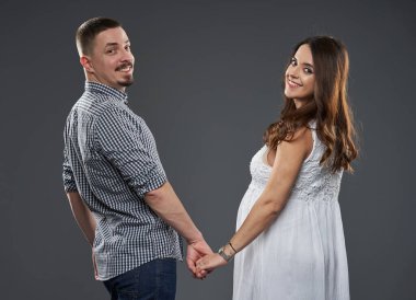 Mutlu bir çiftin el ele tutuşmasını ve neşeli bir ifadeyle geriye bakmasını bekliyorum. Gri arka plana karşı, bebeklerinin sevgi ve beklentilerini sembolize ediyorlar.