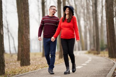 Mutlu bir çift parkta el ele yürüyen bir bebek bekliyor. Seçici bir odak noktasıyla vurulmuş.