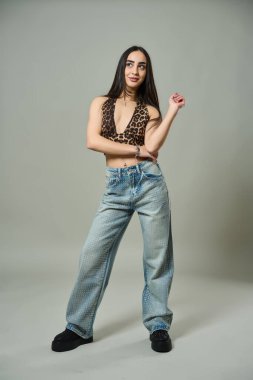 Şık bir kadın, leopar desenli bir bluz ve elmaslı kotla, platform ayakkabıları giyerek rahatça poz verir.