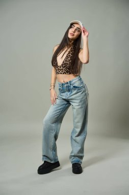 Leopar desenli bluzlu şık bir kadın, elmaslı kotlar ve ters kepli bir kadın neşeli bir jest yapar.