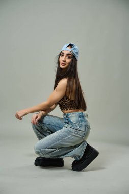 Leopar desenli bluz giyen güzel bir kadın, elmaslı kotlar ve kendine güvenen bir ifadeyle çömeliyor.