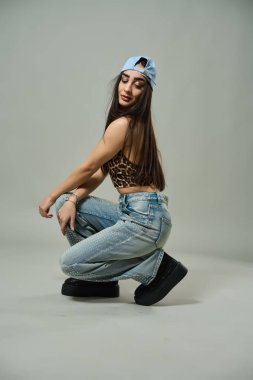 Leopar desenli bluz giyen güzel bir kadın, elmaslı kotlar ve kendine güvenen bir ifadeyle çömeliyor.