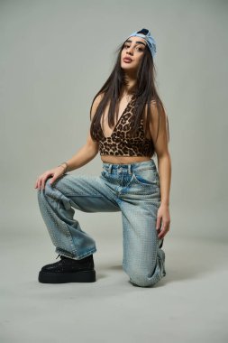 Leopar desenli bluz, yapay elmas kotlu çekici bir kadın ve kendine güvenen bir ifadeyle çömeliyor.