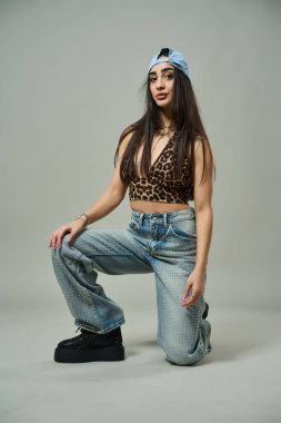 Leopar desenli bluz, yapay elmas kotlu çekici bir kadın ve kendine güvenen bir ifadeyle çömeliyor.
