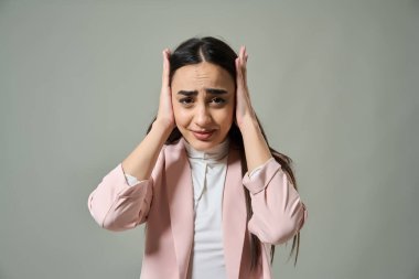 Başını endişeli ve stresli bir ifadeyle gri arka planda tutan genç bir kadın. 