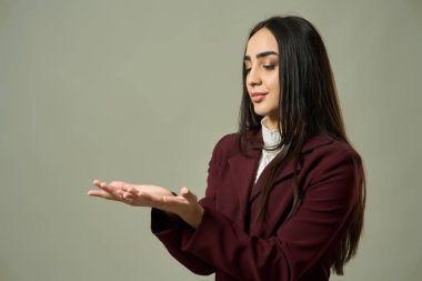 Gri arkaplana karşı düşünceli bir ifadeyle eline bakan genç bir kadın. 