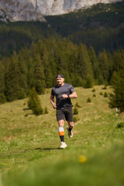 Orman ve arka planda kayalık tepelerle çevrili bir dağ yolunda koşan bir adam.