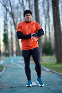 Spor kıyafetli bir adam kışın parkta koştuktan sonra akıllı bakışlarını kontrol ediyor.