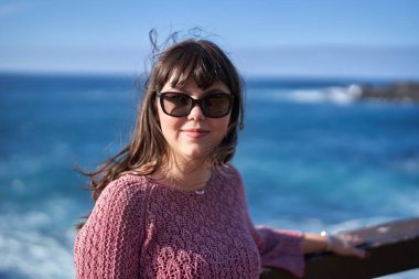 Tenerife 'de okyanusun kenarında gülümseyen güneş gözlüklü ve esintili bir kadın.