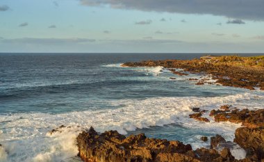 Dalgalar gün batımında engebeli kayalarla engebeli bir volkanik kıyıya çarpıyor.