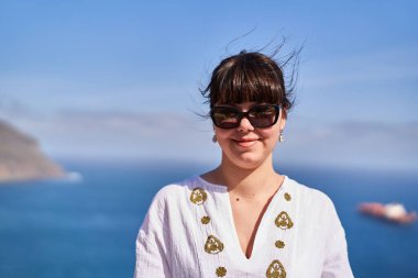 Güneş gözlüğü takan gülümseyen bir kadın ve Tenerife 'nin arka planında uzak bir gemi olan beyaz işlemeli bir elbise.