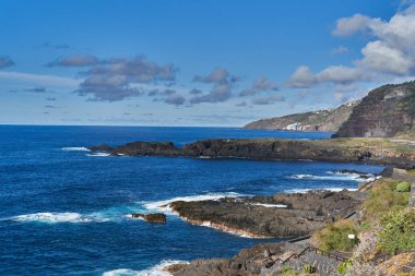 Dalgalar gün batımında engebeli kayalarla engebeli bir volkanik kıyıya çarpıyor.