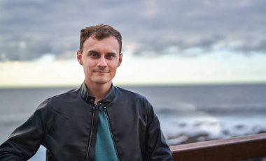 Siyah deri ceket giyen genç bir gezgin Tenerife 'de kayalık bir kıyıya vuran dalgalarla okyanusun kenarında duruyor.