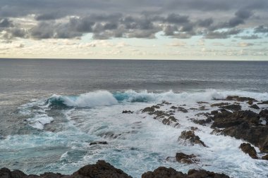 Dalgalar gün batımında engebeli kayalarla engebeli bir volkanik kıyıya çarpıyor.