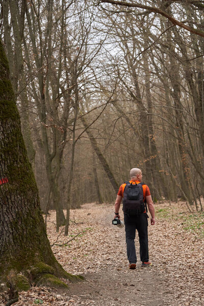 Man carrying a camera with a telephoto lens while walking on a forest trail