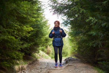 Yoğun orman patikalarında tek başına yürüyüş yapan bir kadın sırt çantası ve açık hava kıyafetleri giyiyor.