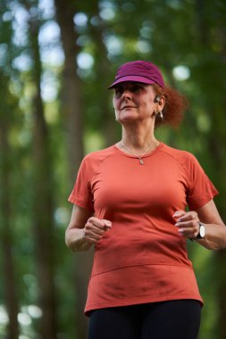Ormanda koşan turuncu gömlekli ve kulaklıklı mor şapkalı bir kadının yakın çekimi.