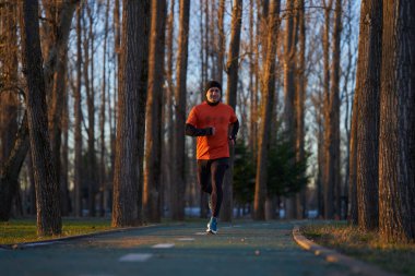 Bir kış sabahı spor kıyafetleriyle parkta koşan bir adam.