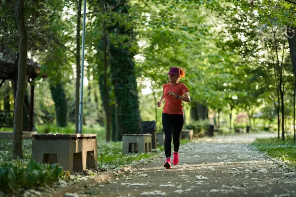 Güneşli bir yaz gününde yapraklı park yolunda koşan bir kadın.