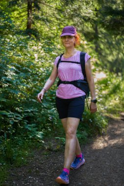 Yeşil ve güneş ışığıyla çevrili ormanda tek başına yürüyen bir kadın.