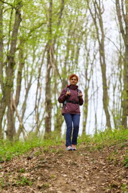 Kızıl saçlı, olgun bir kadın. Sırt çantasıyla geziyor. Dar bir patikada bereketli bahar ormanlarında.