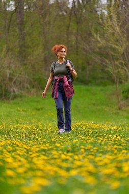 Sarı karahindiba ve yemyeşil çiçeklerle dolu bir çayırda yürüyüş yapan bir kadın.