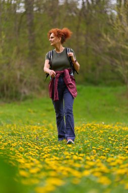 Sarı karahindiba ve yemyeşil çiçeklerle dolu bir çayırda yürüyüş yapan bir kadın.