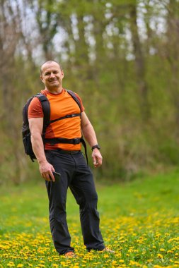Elinde telefonla gülümseyen yürüyüşçü karahindiba dolu bir bahar çayırında yürürken