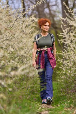 Kızıl saçlı kadın dar bir patikada yürüyor ilkbaharda açan yoğun siyah dikenli çalıların arasında.