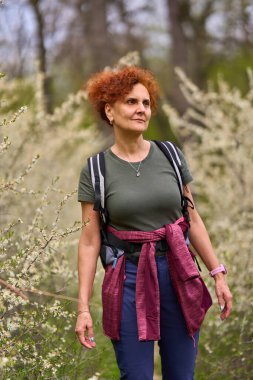 Kızıl saçlı kadın dar bir patikada yürüyor ilkbaharda açan yoğun siyah dikenli çalıların arasında.