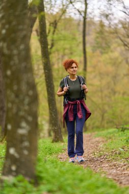 Bir bahar günü sessiz bir orman patikasında yalnız başına yürüyüş yapan bir kadın.