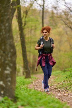 Kızıl saçlı kadın bahar günü ormanda yalnız başına yürüyüş yapıyor.