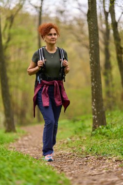 Kızıl saçlı kadın bahar günü ormanda yalnız başına yürüyüş yapıyor.