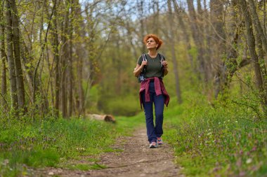 Bir bahar günü sessiz bir orman patikasında yalnız başına yürüyüş yapan bir kadın.