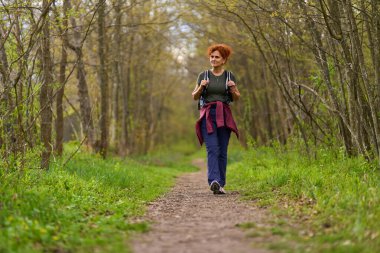 Kıvırcık dişi sırt çantalı gezgin bir bahar günü sakin bir orman patikasında tek başına yürüyüş yapıyor.