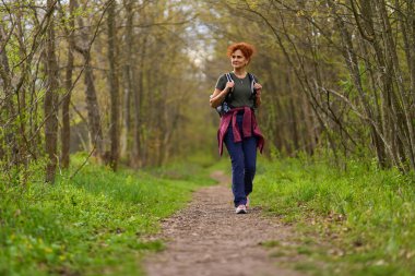 Bir bahar günü ormanda yalnız başına yürüyüş yapan bir kadının portresi.