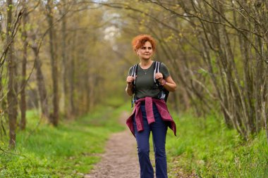 Kızıl saçlı kadın bahar günü ormanda yalnız başına yürüyüş yapıyor.
