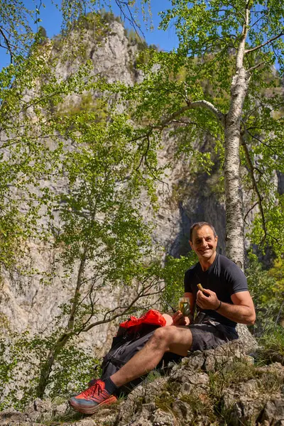 Gülen adam bir huş ağacının altında kayalık bir yamaçta oturmuş çerez yiyor ve yaz yürüyüşü sırasında elinde kavanozla geziyordu.