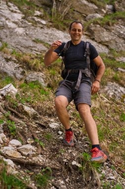 Dik bir yamaçtan inen bir adam yürüyüş kıyafetleri ve kırmızı patika koşu ayakkabıları giyiyor.
