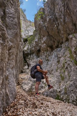 Uzun kaya duvarlarıyla çevrili dar bir kireçtaşı vadisinin ortasında duran gülümseyen bir yürüyüşçü.