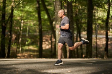 Olgun bir adam doğal ortamdaki antrenman sırasında kaldırımlı orman yolunda koşuyor.