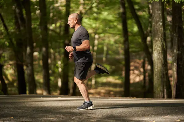 Olgun bir adam doğal ortamdaki antrenman sırasında kaldırımlı orman yolunda koşuyor.