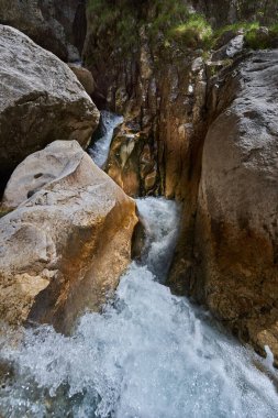 Dik taş oluşumlarından akan suyla dar kayalık vadi.